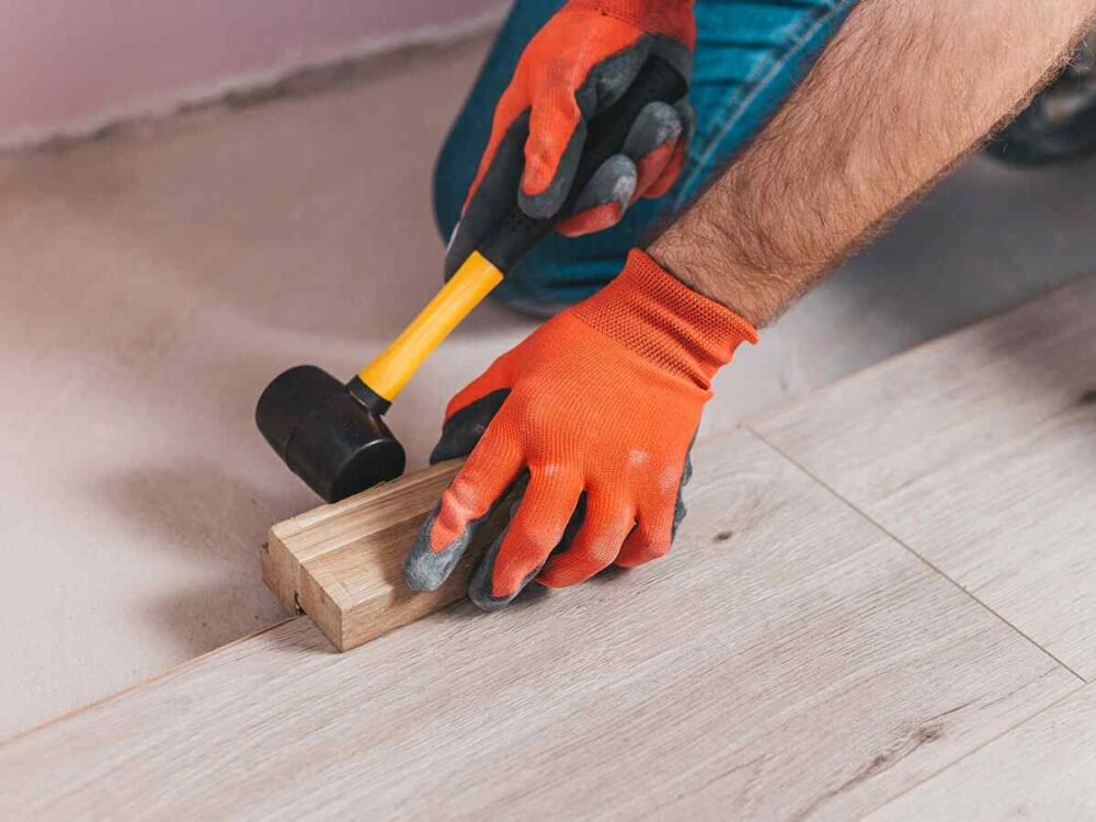 Worker installing laminate flooring with hammer and spacer